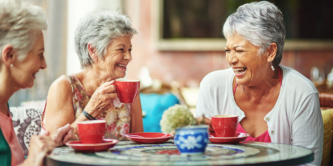 three senior friends laughing over coffee