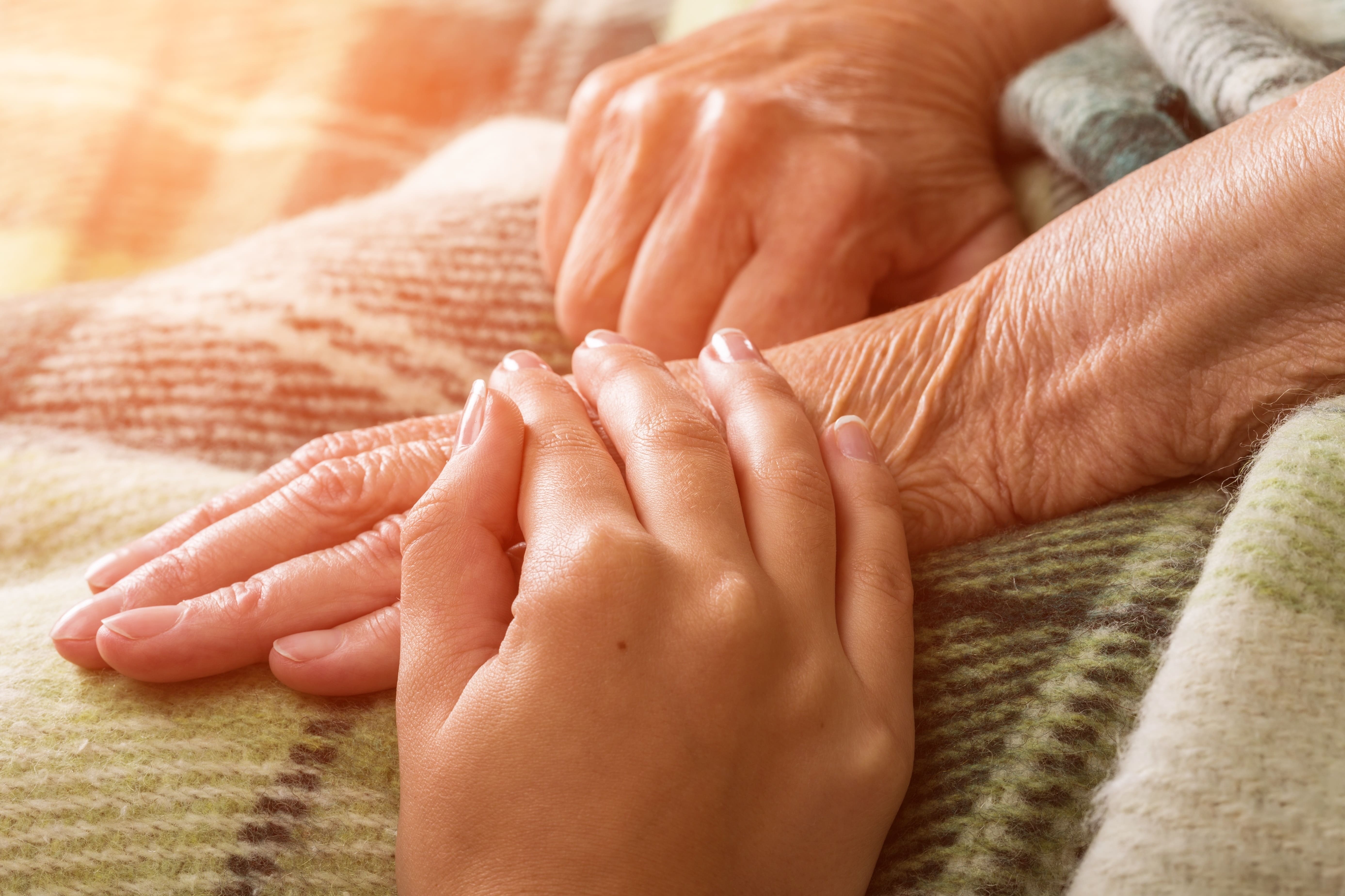 Younger hand laying on top of an older hand with a caring touch