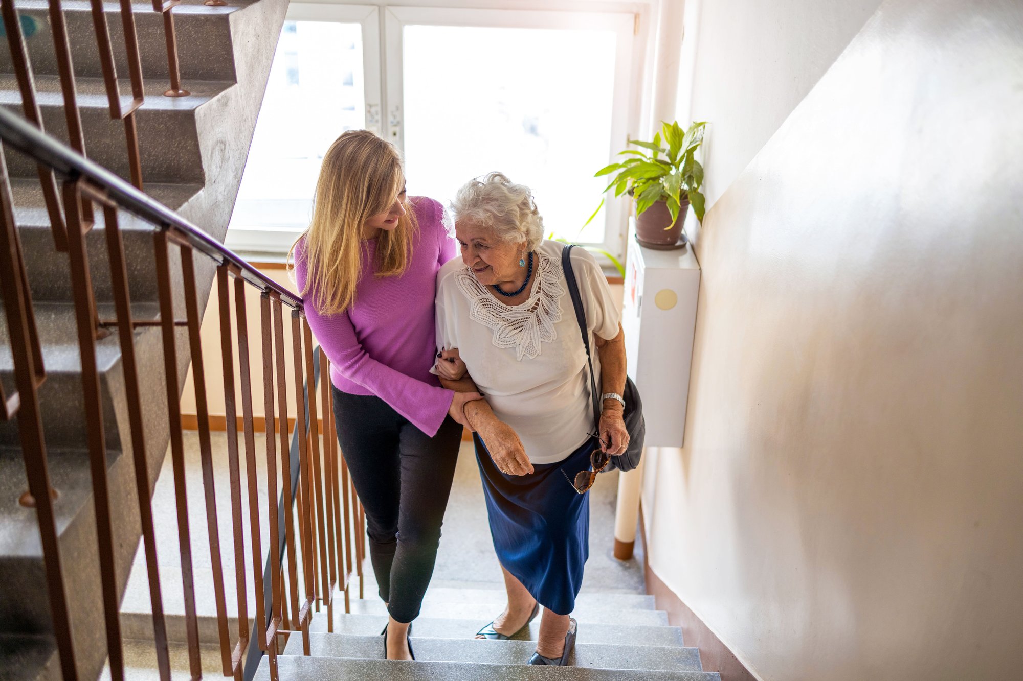 Daughter helping her older mother up the stairs