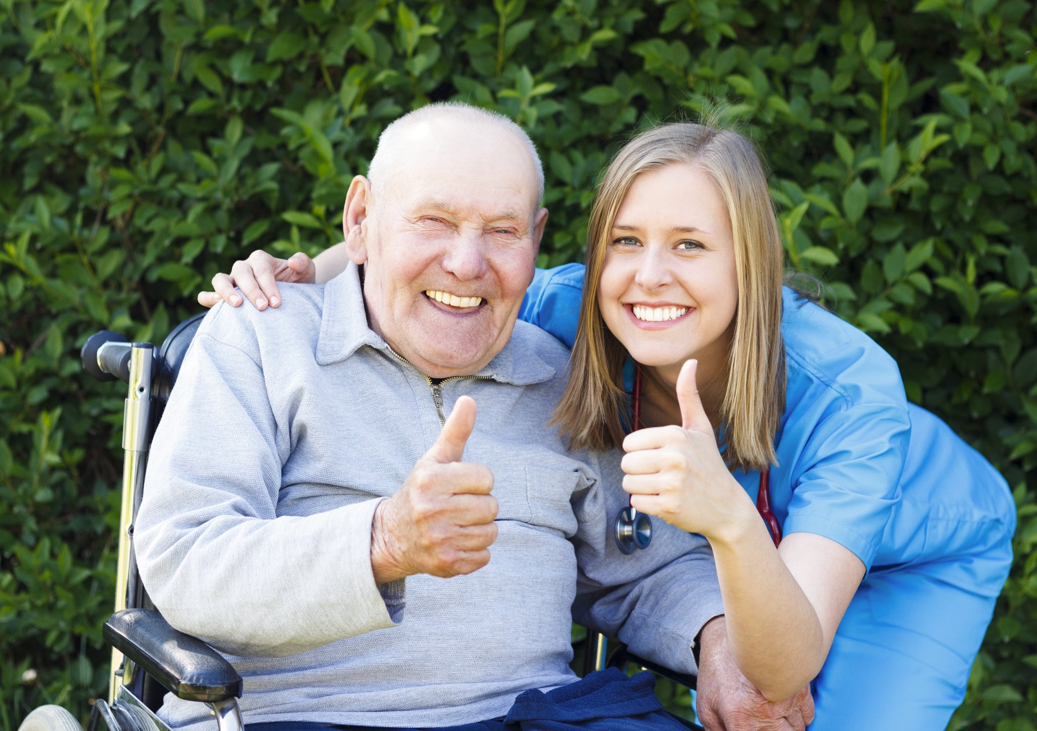 Elderly man and caregiver smiling and giving thumbs up