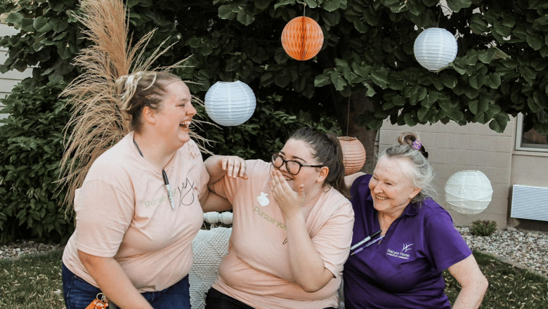 Three team members laughing together on an outdoor bench