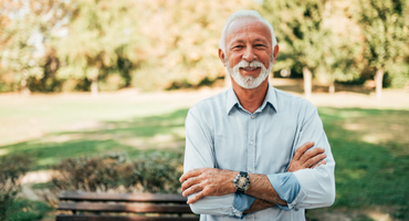 smiling senior man in park with arms crossed