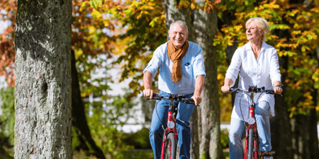 A man and woman riding bicycles with fall leaves behind them