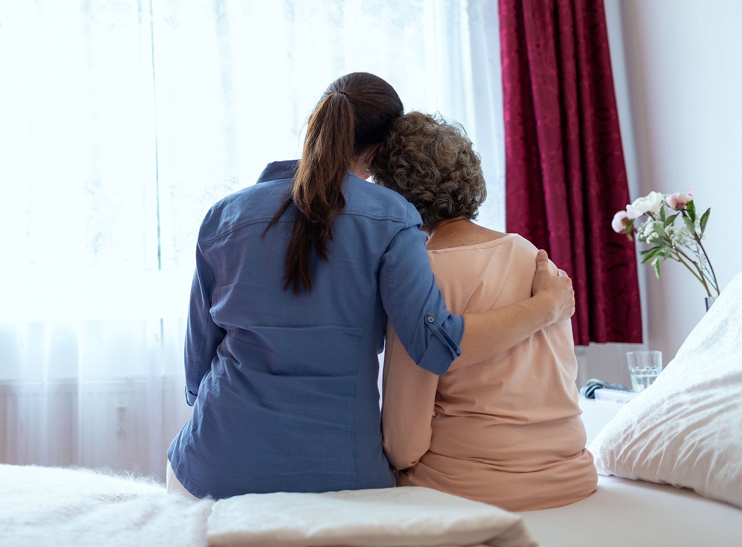 Female home nurse hugging elderly woman on bed